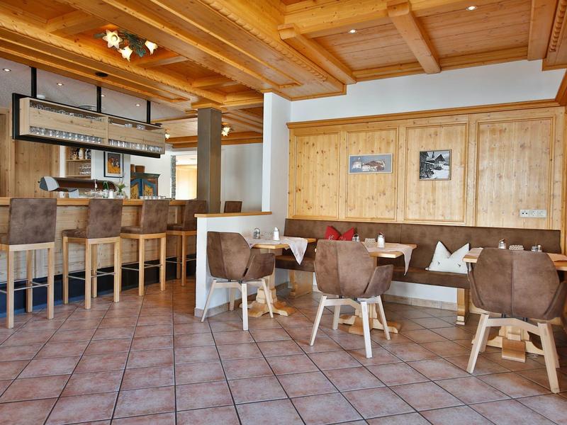 Helles Hotelrestaurant mit Holzmöbeln, Fliesenboden und Bartheke mit Hockern.