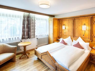 Gemütliches Hotelzimmer mit Doppelbett, Holzverkleidung und einem Sessel neben Fenster und Tisch.