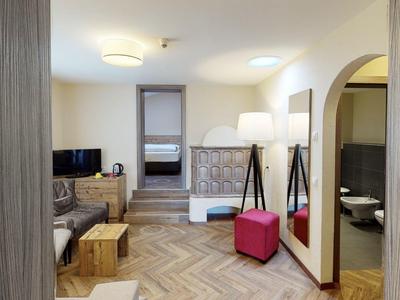 Helles Hotelzimmer mit Sofa, Teppichboden, Hockern und Zugang zu Schlafzimmer und Bad.