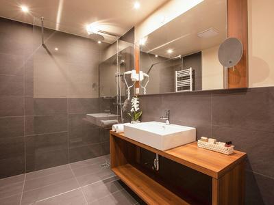 Modernes Badezimmer mit Holzwaschtisch, weißem Waschbecken, Spiegel und grauen Fliesen an Wand und Boden.