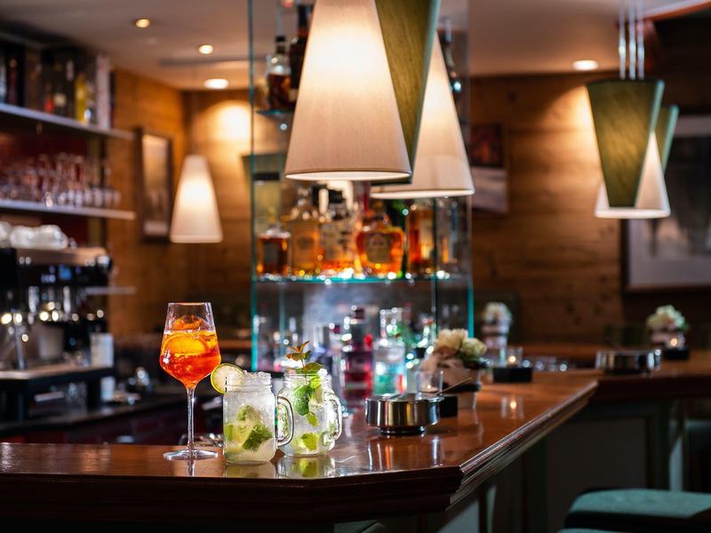 Moderne Bar mit Holztheke, beleuchteten Hängelampen und bunten Getränken auf dem Tresen.