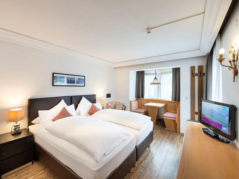 Helles Schlafzimmer mit Doppelbett, Holzboden, Sitzecke am Fenster und TV auf Kommode.