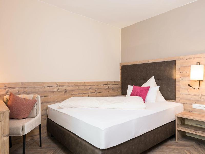 Einladendes Schlafzimmer mit großem Doppelbett, Holzmöbeln und warmem Licht an Wänden.