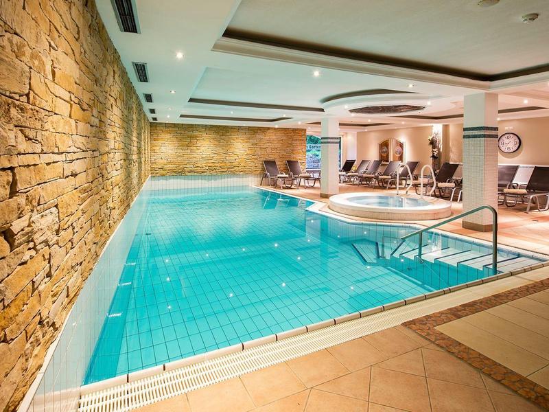 Innenpool mit blauem Wasser, Steinwand links, Holzboden und moderner Beleuchtung.