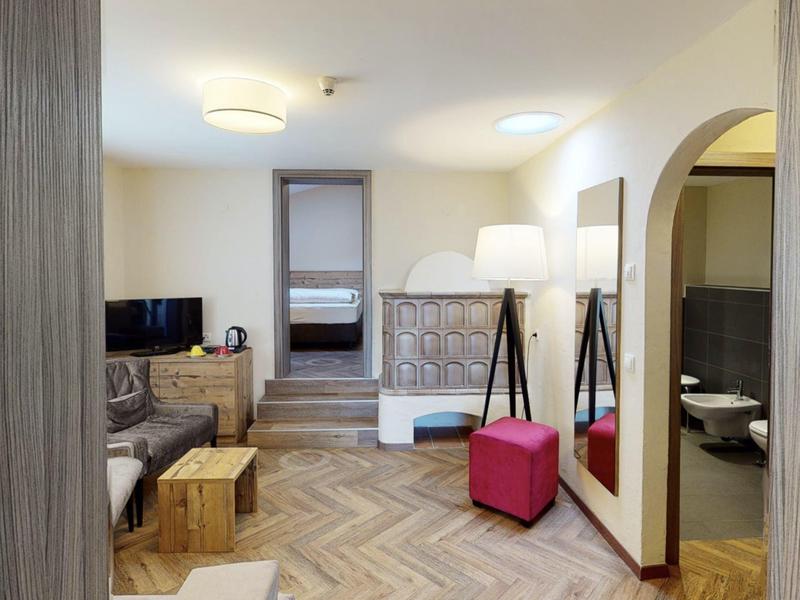 Helles Hotelzimmer mit Sofa, Teppichboden, Hockern und Zugang zu Schlafzimmer und Bad.