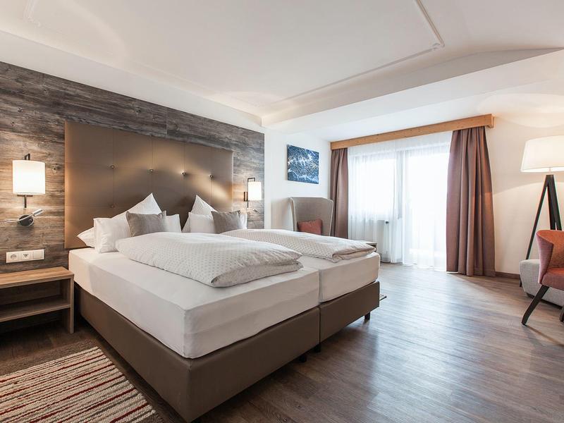 Modernes Hotelzimmer mit großem Bett, Holzboden und Sitzbereich mit Stuhl und Tisch.