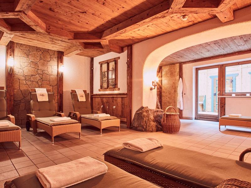 Gemütlicher Wellnessraum mit Holzbalkendecke, Tagesbetten und warmem Licht, offen zum Außenbereich.