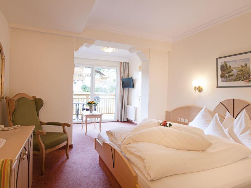 Helles Hotelzimmer mit Doppelbett, Sitzecke und Balkon mit Blick ins Freie.