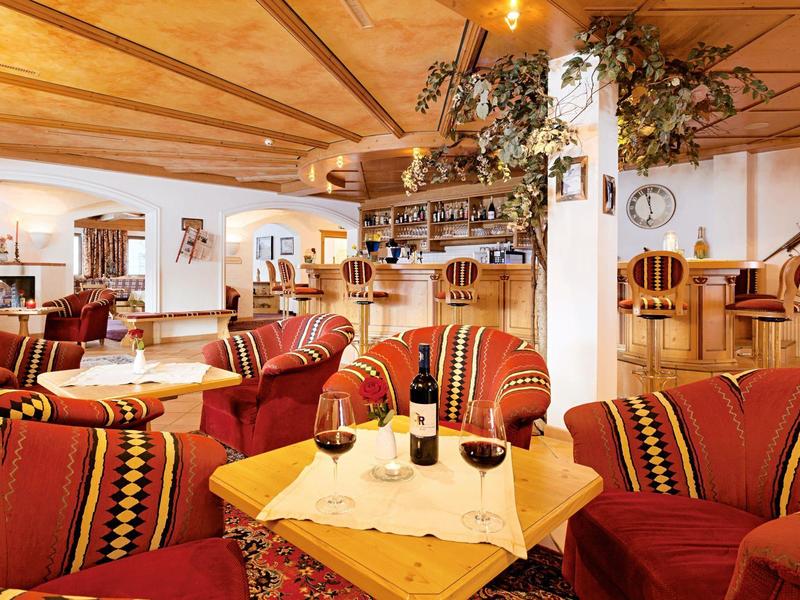 Gemütliche Hotellounge mit rotgemusterten Sofas, Holzmöbeln und Wein auf dem Tisch.