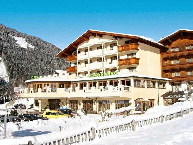 Großes Hotel mit Holzbalkonen, umgeben von verschneiter Berglandschaft und klarem Himmel.