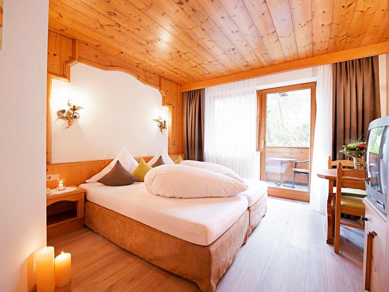 Gemütliches Hotelzimmer mit Holzboden, Doppelbett, Balkon und TV.