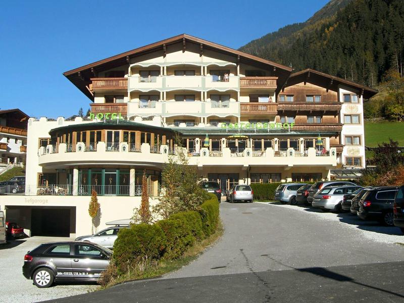 Großes Hotelgebäude mit Balkonen, umgeben von Autos und Bergen bei klarem Himmel.