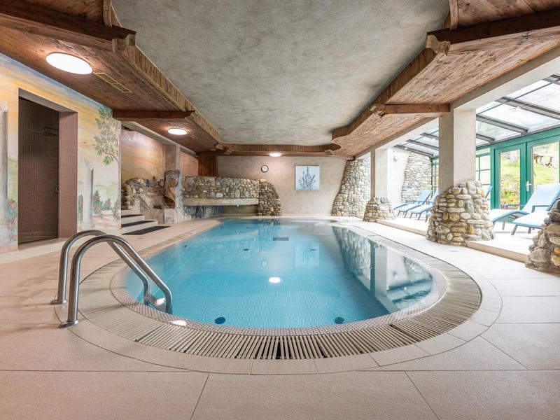 Innenraum mit rechteckigem Schwimmbecken, hellem Fliesenboden und rustikalen Steinwänden.