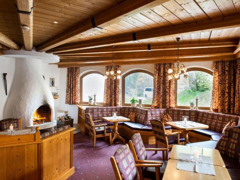 Gemütlicher Gastraum mit Holzbalkendecke, Kachelofen, Holzmöbeln und karierten Sesseln.