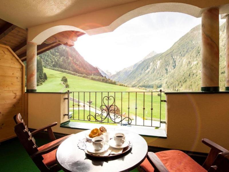 Balkon mit Holzmöbeln und Frühstück, Blick auf grüne Wiesen und Berge bei sonnigem Wetter.