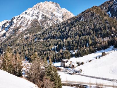 Verschneite Berge mit Wald und kleinen Häusern unter klarem blauem Himmel.