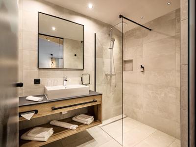 Modernes Badezimmer mit gläserner Dusche, großem Spiegel und dunklem Holzregal unter dem Waschbecken.