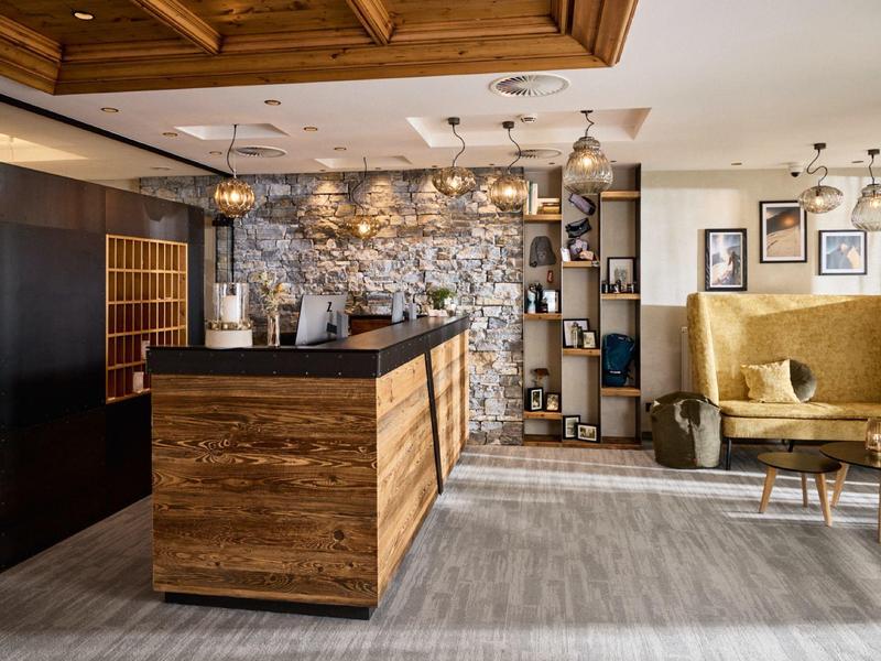 Moderne Wohnküche mit Holzinsel, goldenen Sesseln und dekorativer Steinwand im Hintergrund.