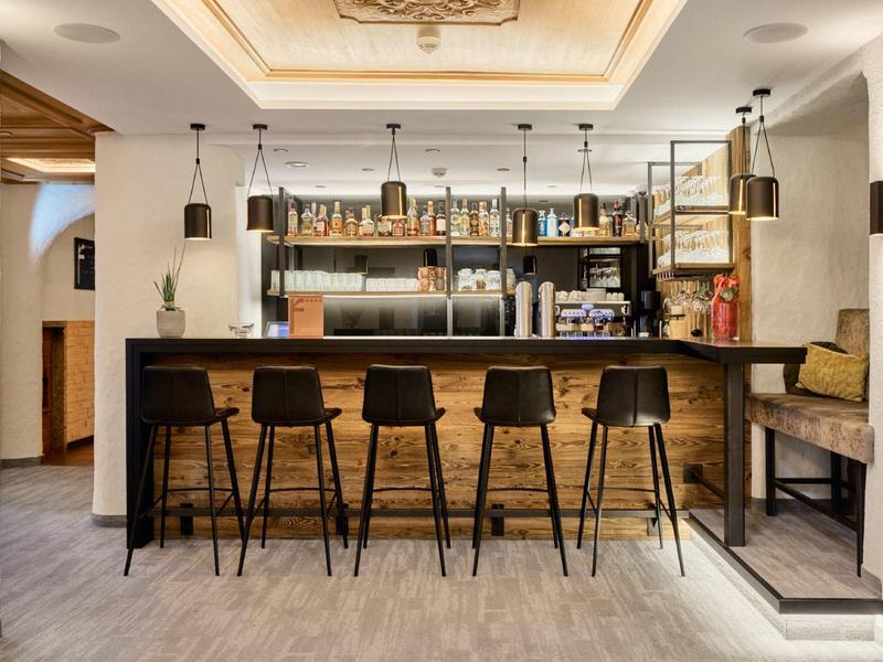 Moderner Bartresen mit fünf schwarzen Hockern, Holzverkleidung und Regalen voller Flaschen.