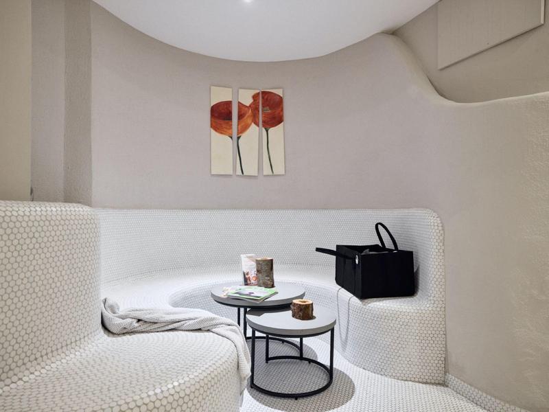 Gemütliche Sitzecke mit weißem Polstersofa, zwei runden Tischen und abstrakter Wandkunst.