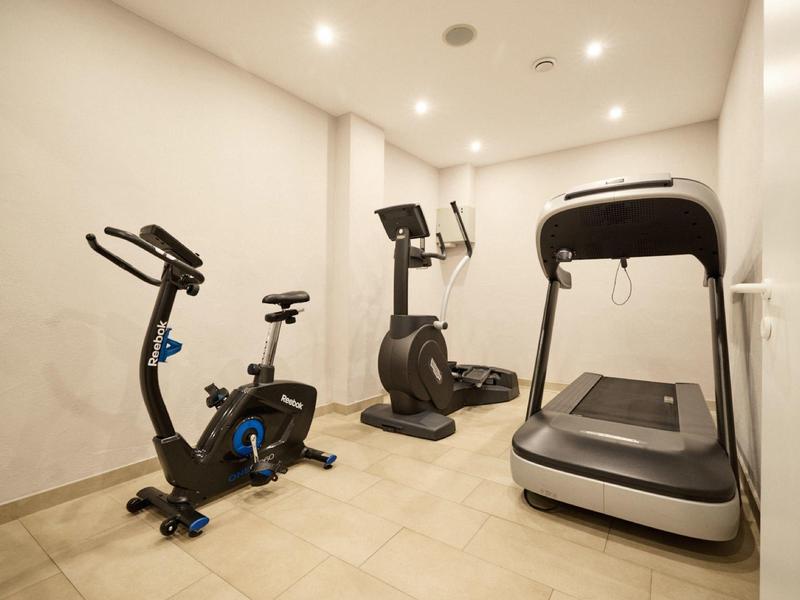 Kleiner Fitnessraum mit Ergometer, Heimtrainer und Laufband, beige Wände und Bodenfliesen.