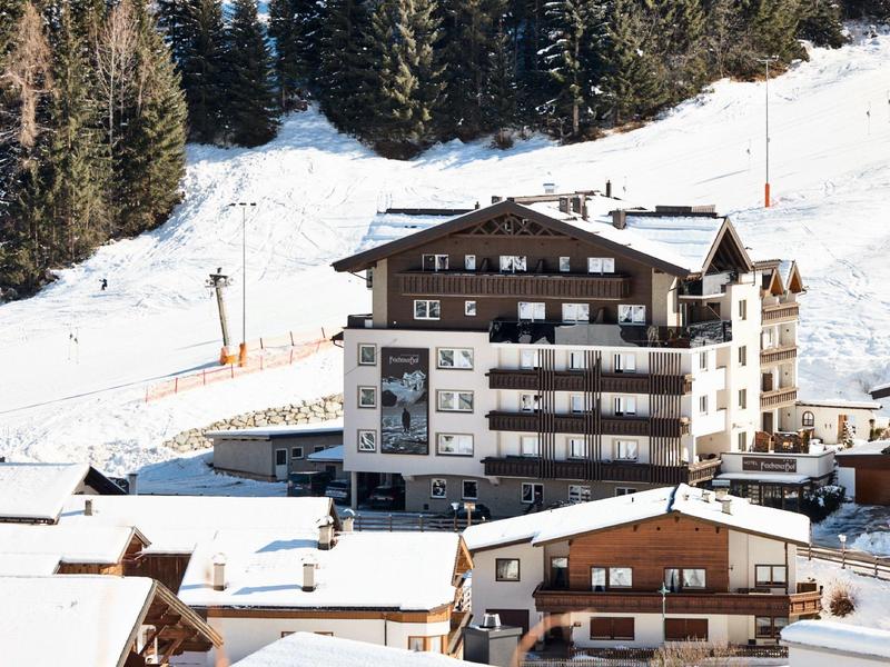 Mehrstöckiges Hotelgebäude in verschneiter Berglandschaft mit Nadelbäumen im Hintergrund.