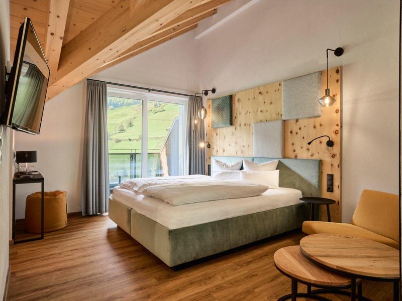 Ein gemütliches Schlafzimmer mit Holzboden, großem Bett, Holzdecke und Balkon mit Bergblick.