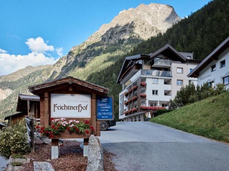 Bergdorf mit Almwiese, mehrstöckigen Häusern und bewaldetem Berg unter blauem Himmel.