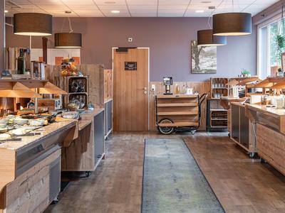 Modernes Buffet mit Holzmöbeln, warmem Licht und großen Fenstern in einem hellen Raum.