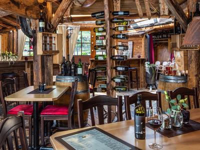 Gemütliches Restaurant mit Holzbalken, Tischen, Weingläsern und Weinflaschen in warmem Licht.