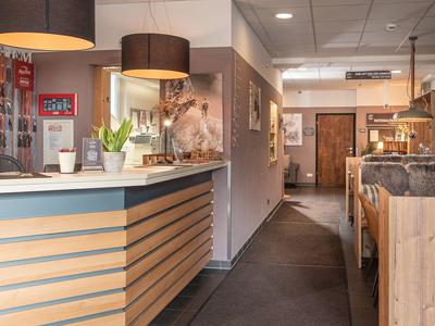 Hotelrezeption mit modernem Holztresen, zwei dunkelbraunen Lampen und Flur zu den Gästezimmern.