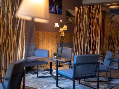 Lounge d'hotel moderna con decorazioni in legno, poltrone blu e illuminazione calda.