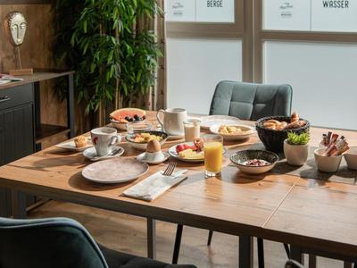 Holztisch mit gedecktem Frühstück, Stühlen, Pflanzen und Schrank im modernen Esszimmer.