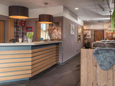 Area reception con bancone moderno, due grandi lampade a sospensione e zona attesa confortevole in legno.