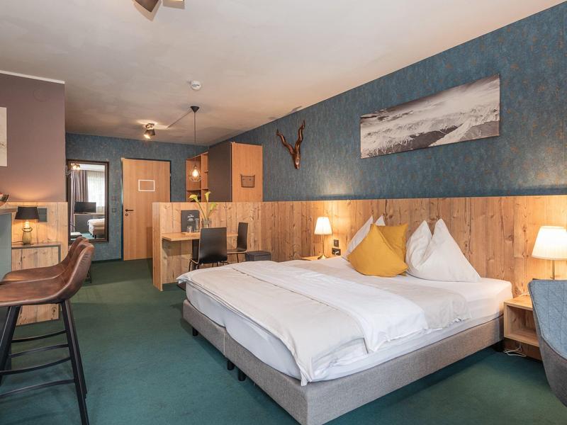 Gemütlich eingerichtetes Schlafzimmer mit blau-beiger Wand, Doppelbett, Teppich und Barhockern.