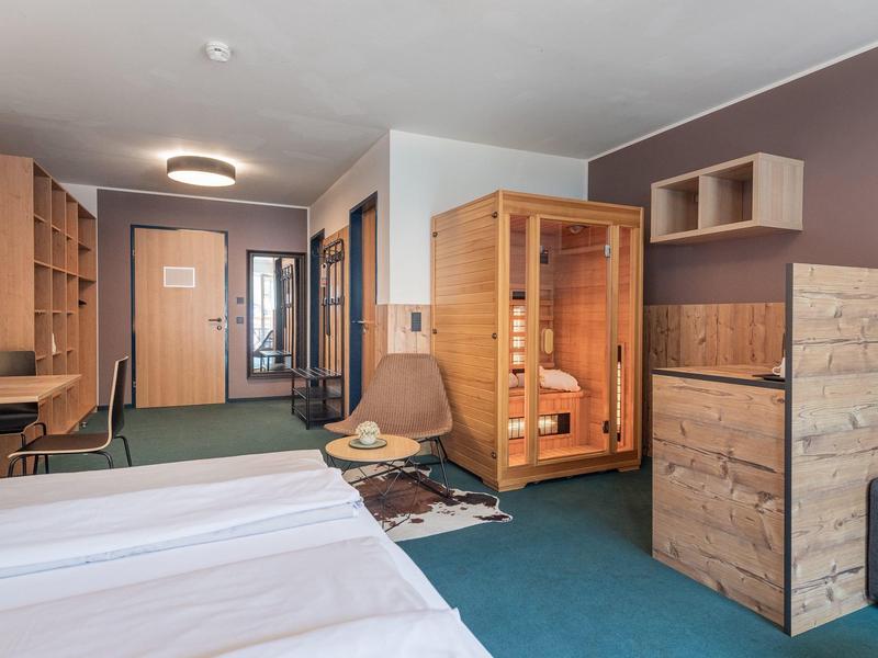 Modern eingerichtetes Hotelzimmer mit Doppelbett, Saunakabine, Sitzbereich und Holzmöbeln.
