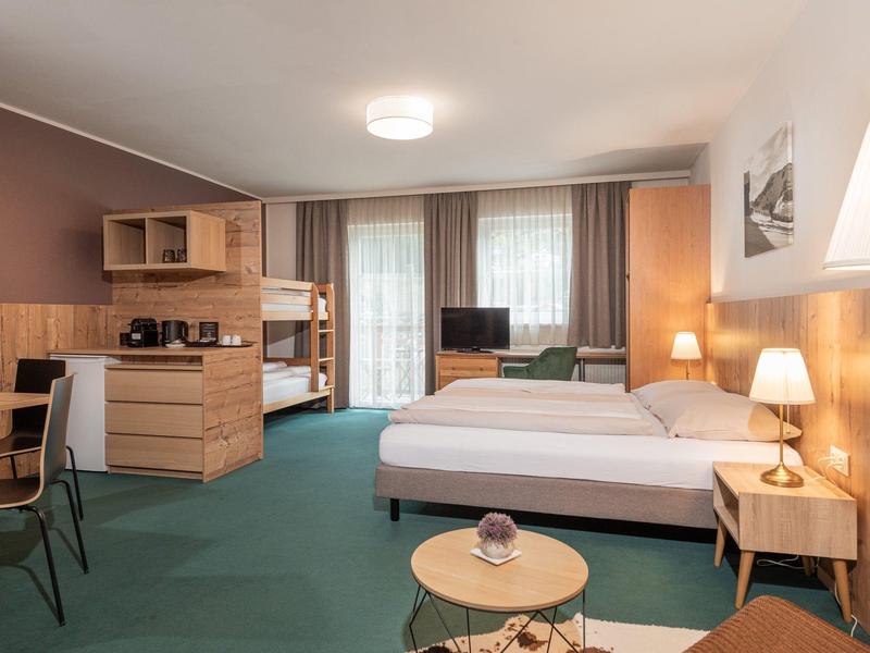 Geräumiges Hotelzimmer mit Doppelbett, Etagenbett, Sitzbereich, Schreibtisch und großem Fenster.