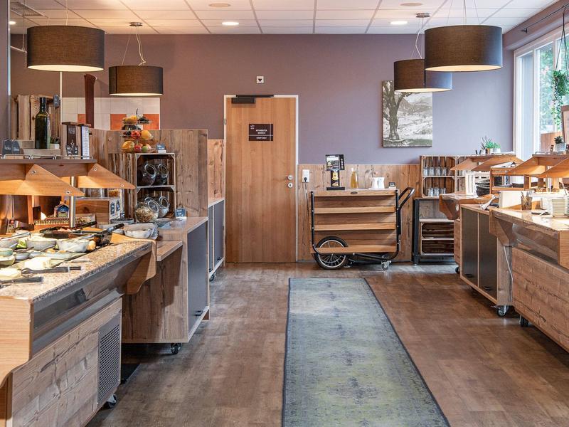 Modernes Buffet mit Holzmöbeln, warmem Licht und großen Fenstern in einem hellen Raum.