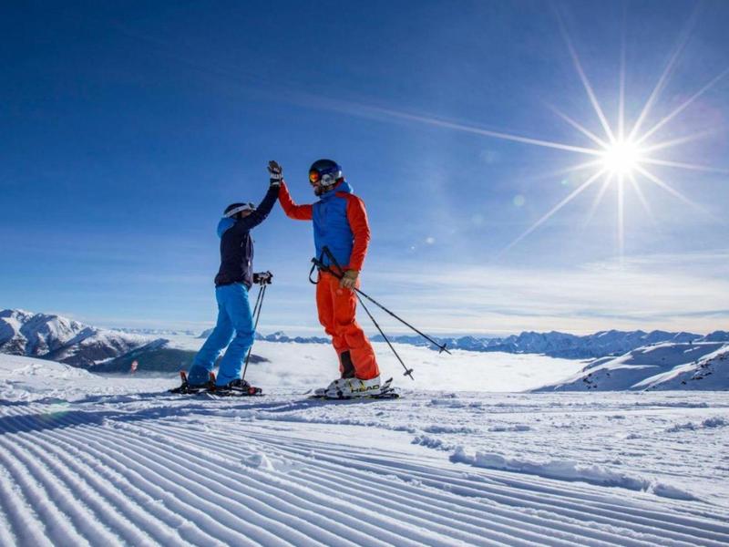Zwei Skifahrer geben sich auf der Piste in sonniger Berglandschaft einen High-Five.
