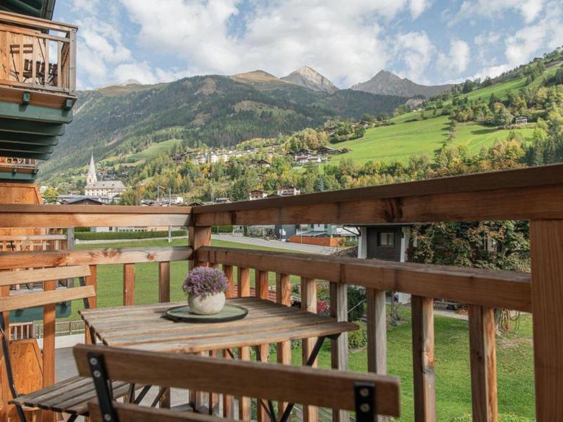 Holzterrasse mit Tisch und Stühlen, Berglandschaft und grünen Wiesen im Hintergrund bei Tageslicht.