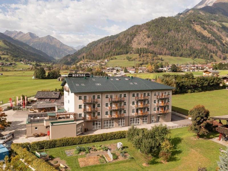 Großes Hotelgebäude in einem grünen Tal, umgeben von Bergen und Feldern unter bewölktem Himmel.