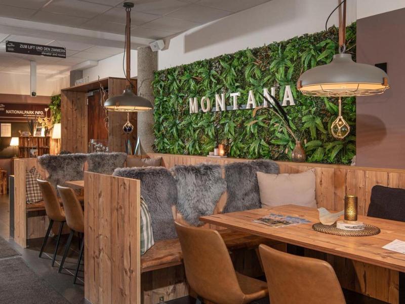 Gemütliches Restaurant mit Holzmöbeln, grüner Wanddeko und warmem Lichtdesign.