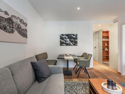 Helles Wohnzimmer mit grauem Sofa, dunklem Tisch, Stühlen und moderner Fotokunst an der Wand.