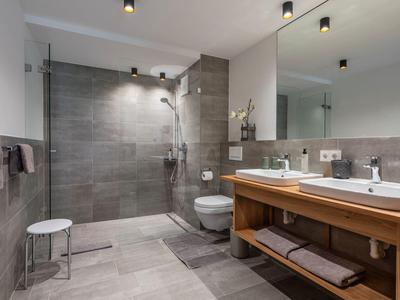 Modernes Badezimmer mit großer begehbarer Dusche, Doppelwaschbecken und Holzunterschrank.