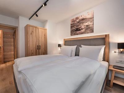 Modernes Schlafzimmer mit großem Bett, Holzmöbeln, weißer Wand und gedämpfter Beleuchtung.