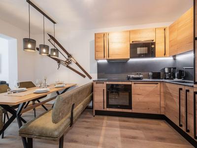 Moderne Küche mit Holzmöbeln, schwarzem Backofen, grauer Arbeitsplatte und Esstisch mit Bank und Stühlen.