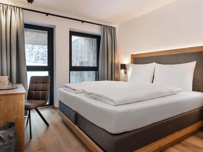 Gemütliches Schlafzimmer mit großem Bett, Holzmöbeln und Fenster mit grauen Vorhängen.