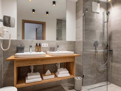 Modernes Badezimmer mit Holzwaschtisch, großen Spiegeln, grauen Fliesen und Glas-Dusche.