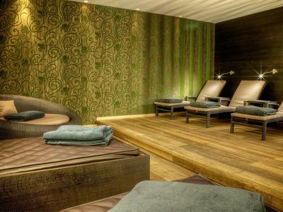 Gemütlicher Spa-Ruhebereich mit bequemen Liegen, Holzboden und grüner, gemusterter Wandgestaltung.