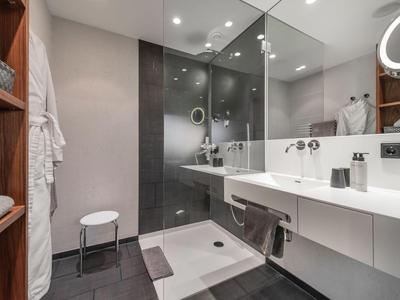 Moderne Badezimmer mit weißem Waschtisch, Glas-Duschkabine, Holzregalen und graßfarbenen Fliesen.